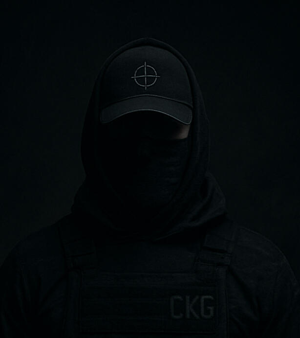 C.K. Grady: anonymous figure in black, wearing a ball cap marked with a sniper crosshair and a hoodie labelled "CKG". His face is mostly obscured by shadows and a tactical buff, revealing only his eyes - focused and unreadable. The image embodies stealth,